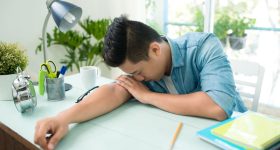 Stressed overworked man studying sleepy on desk.