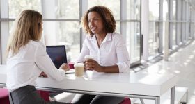 Two young businesswomen at a meeting talking, close up