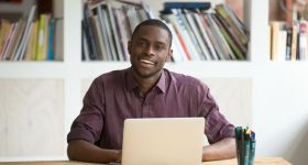 African-american businessman sitting at desk with laptop looking