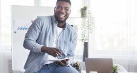 Cheerful black employee using digital tablet in office and laughing