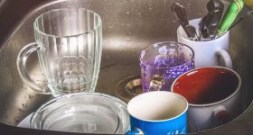 Dirty dishes in foam in the sink waiting for washing. Mugs, plates, cutlery.