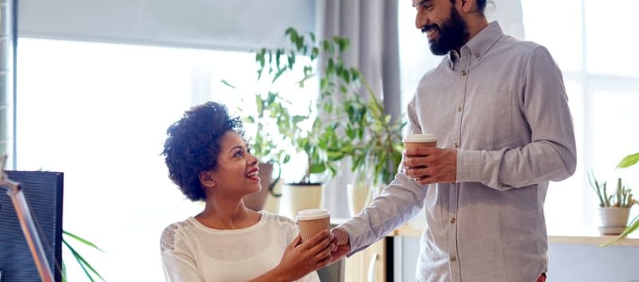 happy man bringing coffee to woman in office